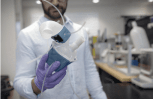 Man holding 3d printed heart. Half is blue and half is white. Clear tubes are stemming from the model to represent arteries.