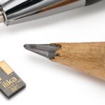 A small, flat, rectangular Stereax battery with a pencil tip and ballpoint pen for scale.