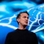 A photo of Synchron co-founder and CEO Dr. Tom Oxley giving a TED Talk with an image of the Stentrode device displayed behind him.