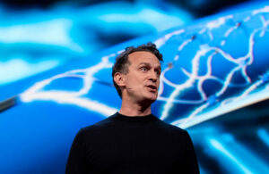 A photo of Synchron co-founder and CEO Dr. Tom Oxley giving a TED Talk with an image of the Stentrode device displayed behind him.