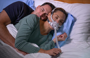 A marketing photo of a woman wearing a ResMed AirFit F40 CPAP mask and sleeping on her side.