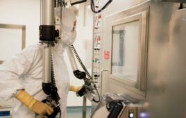 A photo of a BWXT Medical employee in protective gear dispensing radioactive TheraSphere beads inside a shielded "hot cell" using manual manipulators.