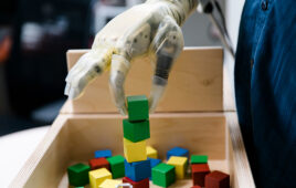 A patient stacks wooden blocks using a DEKA advanced prosthetic arm and hand.
