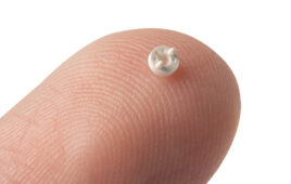 A photo of a tiny micromolded medical device component on a fingertip.