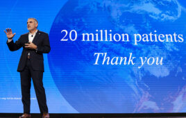 A photo of Intuitive CEO Dave Rosa on stage with "20 million patients thank you" on screen behind him.
