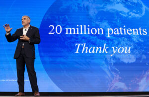 A photo of Intuitive CEO Dave Rosa on stage with "20 million patients thank you" on screen behind him.