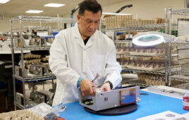 An image of an employee wearing a lab coat working in a manufacturing facility.
