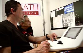 A photo of a surgeon using XCath's Iris robotic system to perform a remote thrombectomy on a patient not in the room.