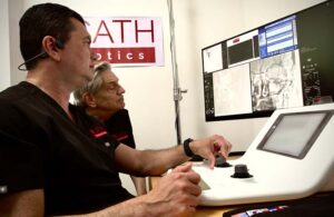 A photo of a surgeon using XCath's Iris robotic system to perform a remote thrombectomy on a patient not in the room.