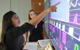 A photo of Suchi Saria pointing at the Bayesian Health Sepsis Flagging Device technology.