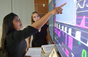 A photo of Suchi Saria pointing at the Bayesian Health Sepsis Flagging Device technology.